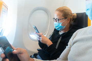 Image showing A young woman wearing face mask, using smart phone while traveling on airplane. New normal travel after covid-19 pandemic concept.