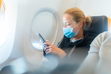 Image showing A young woman wearing face mask, using smart phone while traveling on airplane. New normal travel after covid-19 pandemic concept.