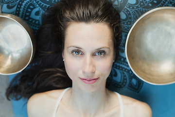 Image showing Yoga concept, meditation and sound therapy. Portrait of beautiful young caucasian woman surrounded by copper tibetan singing bowls and instruments