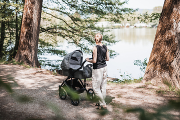 Image showing Rear view of casually dressed mother walking with baby stroller in Koseski bajer city park in Ljubljana, Slovenia. Family, child and parenthood concept.