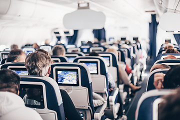 Image showing Interior of airplane with passengers on seats and stewardess in uniform walking the aisle, serving people. Commercial economy flight service concept.