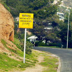 Image showing Signage with warning, road and city with nature, outdoor and board with urban town or funny. Direction, icon or street with symbol, rock or trees with humor or language with bushes, stone or safety