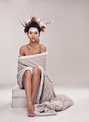 Image showing Woman, fashion and native american headdress in studio with feathers in hair, portrait and culture make up in modern blanket. Model, face and indigenous on box and elegant cloth on grey background