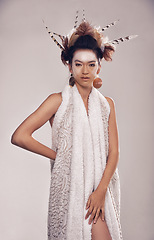 Image showing Model, portrait or culture headdress in studio with feathers, fashion and tribal make up in trendy clothes. Native american woman, face and indigenous cosmetics in robe and elegant on grey background