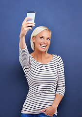 Image showing Happy woman, selfie and photography with phone for picture, moment or capture on a blue studio background. Female person, blonde or model with smile for photo, memory or social media on mockup space