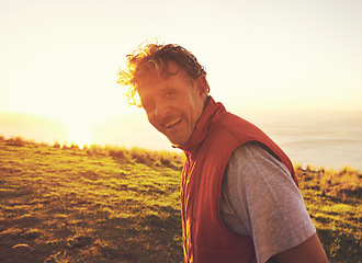 Image showing Sunset, nature and portrait of man by ocean for adventure, relaxing and enjoy weekend outdoors. Happy, smile and person with flare on hill for holiday, vacation and travel destination in evening