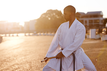 Image showing Serious man, karate and fitness with nunchuck in city for kata, fighting technique or style. Young male person or muay thai fighter with weapon for martial arts or self defense on street in town