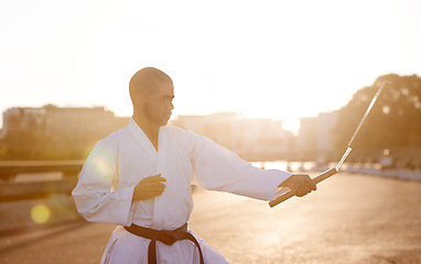 Image showing Man, karate and fitness with nunchuck in city for fighting style, technique or combat skill. Young male person or taekwondo fighter with weapon in martial arts or self defense on street in urban town