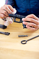 Image showing Hand, cleaning and man with gun equipment at table for safety, self defense and confident handgun assembly. Process, caution and person with firearm maintenance, cloth and wiping dust, dirt and tools