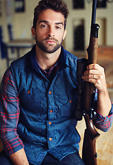 Image showing Hunter, confidence and portrait of man with gun for game shooting, adventure and hobby in home. Sports, trophy hunting and serious face of person in cabin with rifle, pride and sportswear in home