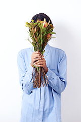 Image showing Woman, bouquet and cover face in studio with leaves, fashion and sustainability by white background. Person, model and mystery with flowers, plants and organic clothes with ecology for environment