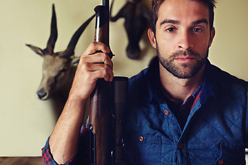 Image showing Hunting, trophy and portrait of man with gun for game shooting, adventure and hobby with confidence. Sports hunter and serious person in cabin with rifle, pride and animal head collection in home