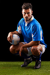 Image showing Rugby, background and portrait of man at night for training, competition or sportswear dark studio. Confident, kneeling and male athlete with ball for professional sport, workout or exercise on grass