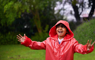 Image showing Rain, celebration and excited boy in a forest for adventure, freedom or exploring games in nature. Winter, travel and happy kid with raincoat in India outdoor for learning, journey or storm surprise