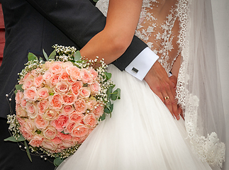 Image showing Bride and groom share an embrace with pink rose bouquet on summe