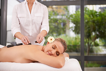 Image showing Woman, hands and hot stone massage at spa with masseuse, flower for natural treatment and wellness with zen. Calm, peace and luxury bodycare with warm rocks for detox, self care and holistic healing
