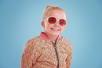 Image showing Happy, sunglasses and girl child in studio with funky, trendy and stylish jacket for outfit. Excited, smile and face of young kid model with cool fashion and accessory isolated by blue background.