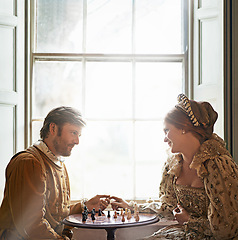 Image showing Renaissance, couple and chess date in home with holding hands, vintage and medieval costume in a palace. Window, luxury and queen together with smile from strategy game and talking with love and care