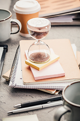 Image showing Crop of hourglass on home office table count measure time.  Workplace of busy employee, time management and burnout concept