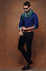 Image showing Fashion, confidence and man or model in studio isolated on a brown background mockup space. Serious, person and roll sleeve on shirt for style in casual clothes, trendy or cool sunglasses with jeans