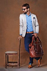 Image showing Bag, chair and confident man with clothes for fashion, style and formal wear isolated on studio background. Male person, gentleman and businessman with trendy outfit, class or suit in brown backdrop