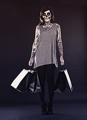 Image showing Woman, skull makeup and shopping bags in studio on dark background with retail and discount for halloween. Portrait, female person and tattoo with edgy or creative style, body art and confidence