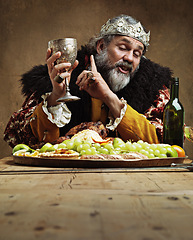 Image showing King, feast and drunk in table with wine glass for dinner on dining hall for tradition, culture and meal in palace. Monarch, leader and eating buffet or supper on royal party as lord with crown.