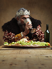 Image showing King, feast and drink wine in table as royalty on dining hall for tradition, culture and meal in palace. Portrait, monarch and leader with eating buffet or supper with chicken in confidence and crown