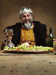 Image showing King, feast and happy in table with wine glass as lord on dining hall for tradition, culture and meal in palace. Portrait, monarch and leader with eating buffet or supper in royal party with crown
