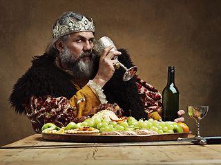 Image showing King, confident and feast at table with wine glass as royalty in studio on brown background for tradition, culture and meal. Portrait, monarch and leader with eating buffet or supper with confidence