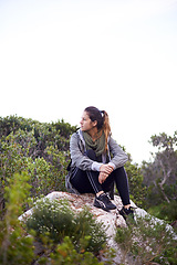 Image showing Woman, sitting and rock for hiking and adventure in nature with sneakers for walking outdoor and break. Young person or hiker and look for view in landscape with bush and plants for exercise and rest