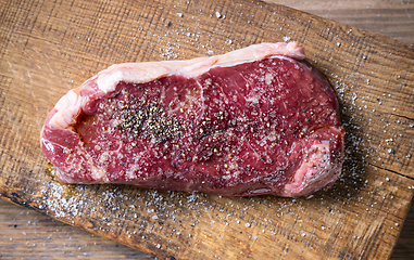 Image showing fresh raw beef steak meat with salt and pepper on wooden cutting