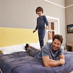 Image showing Happy, jumping and father with kid on bed bonding, playing and having fun together at modern home. Laughing, smile and boy child standing on dad laying in bedroom on weekend at family house in Canada