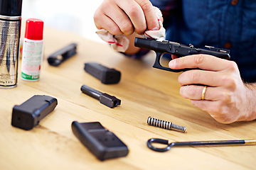 Image showing Hands, man with gun cleaning process at table for safety, self defense and handgun assembly. Caution, equipment and person with firearm maintenance with cloth, magazine and wiping dust, dirt and oil