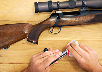 Image showing Hands, cleaning and person with rifle at table for safety, barrel and weapon care or assembly. Process, equipment and man in gun maintenance, cloth and wiping dust, dirt and tools for hunting sports