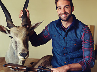 Image showing Hunter, trophy and portrait of happy man with gun for game shooting, adventure and hobby with confidence. Sports hunting and person in cabin with rifle, pride and animal head collection with smile