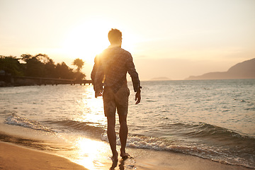 Image showing Man, walking on beach and ocean with sunset, lens flare with back view and waves on vacation in Hawaii. Tourism, travel and adventure with peace, zen and fresh air for wellness, summer and sunshine