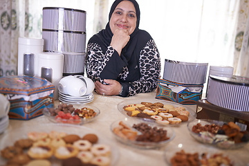 Image showing Mature woman, Islamic and food in house with cheerful, smile and dining table for Iftar. Muslim person, cookie dessert and joy with Eid Mubarak, religion and celebration for breaking fast at home