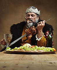 Image showing King, man and food at table with wine as royalty on dining hall for tradition, culture and meal in palace. Monarch, leader and eating buffet or supper with sword for chicken with fruit and luxury