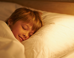 Image showing Boy, pillow and rest for night, sleeping and tired with fatigue and peace. Child, dreaming and exhausted with blanket, bed and bedroom with lamp for serene childhood at home or house for childcare