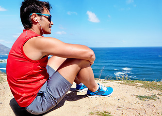 Image showing Runner, man and earphones to relax at beach with rest, break or breathing with music in summer sunshine. Person, listening and streaming with subscription with workout, memory and sitting by ocean