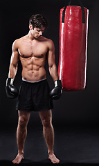 Image showing Boxing, man and training in studio with punching bag for workout, exercise or fight competition with dark background. Gloves, boxer and serious male athlete for confidence, martial arts and fitness