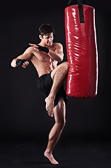 Image showing Man, fighter and boxing bag with kick in studio for self defence workout, martial arts or black background. Male person, wellness and mockup space for strength training with gym, fitness or sport