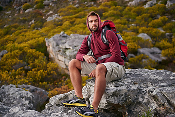 Image showing Man, mountain and hiking in nature for rest and fitness for wellness and exercise for training and adventure in environment. Young person, sitting with backpack on rock for workout and trekking