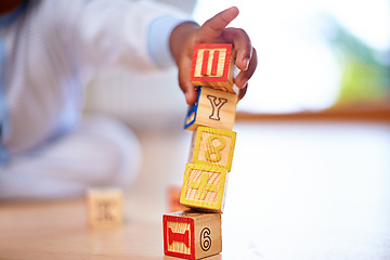 Image showing Wooden blocks, baby and hands on floor in house in living room with toys for motor skills, growth and child development. Children games, kids and ground in home for learning, literacy and playing