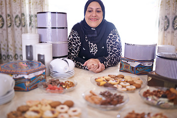 Image showing Woman, Muslim and cakes in house for celebration, cheerful and dining table with food for Iftar in Ramadan. Islamic person, dessert and joy in Eid Mubarak, religion and holiday or event at home