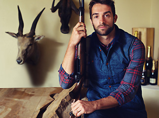 Image showing Hunter, trophy and portrait of man with gun for game shooting, adventure and hobby with confidence. Sports hunting and serious person in cabin with rifle, pride and animal head collection in home