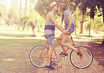 Image showing Couple, kiss and park with bike, date and relaxation for relationship bonding and love. Man, woman and bicycle with nature, grass and care for new york travel and adventure on holiday or honeymoon