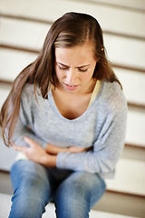 Image showing Stomach pain, stress and woman in a house with pms, gas or constipation, virus or gut health problem. Stairs, belly ache and female person frustrated by endometriosis, crisis or menstruation cramps