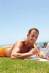 Image showing Man, book and reading on grass in portrait by ocean with knowledge, relax and swimming pool on vacation. Person, cocktail and novel on lawn with pride, topless or outdoor for holiday by sea in Naples